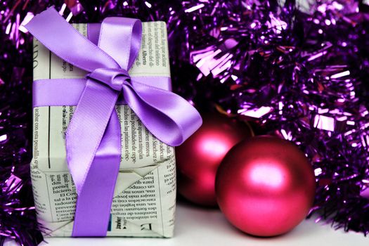 Gifts wrapped in old newspaper with purple tinsel, tie and baubles on white background