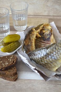 Vodka, dry fish, pickles, black bread on the tablecloth from the newspaper. Vertical image