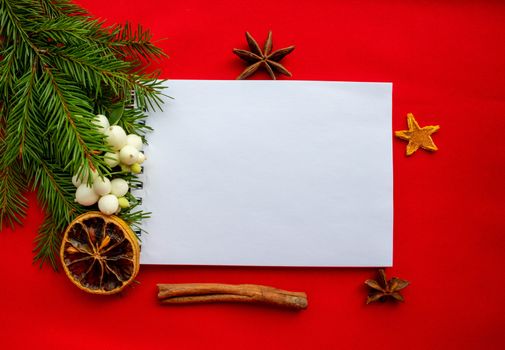 Notepad and green fir branches with white dogwood berries,cinnamon stick,dry lemon on a red background. New year's concept of Christmas.