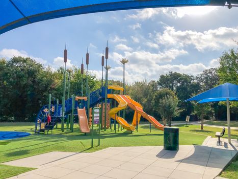 Modern neighborhood playground with sun shade sails, artificial grass in Flower Mound, Texas, America. Suburban recreational facility surrounded by wooden fence and tall trees