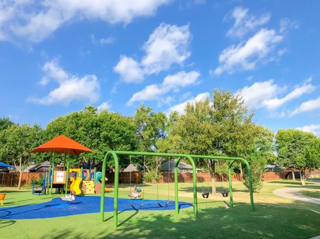 Residential neighborhood playground with sun shade sails and artificial grass in Flower Mound, Texas, America. Suburban recreational facility surrounded by wooden fence