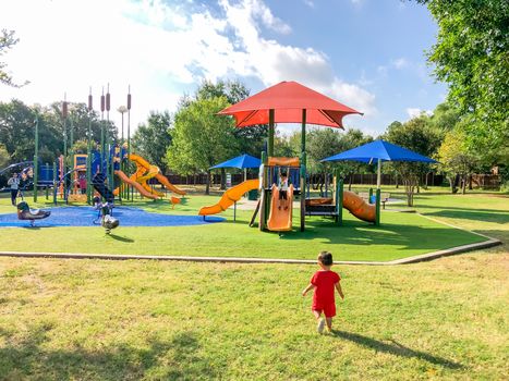 Asian toddler boys playing at residential neighborhood playground with sun shade sails and artificial grass in Flower Mound, Texas, America
