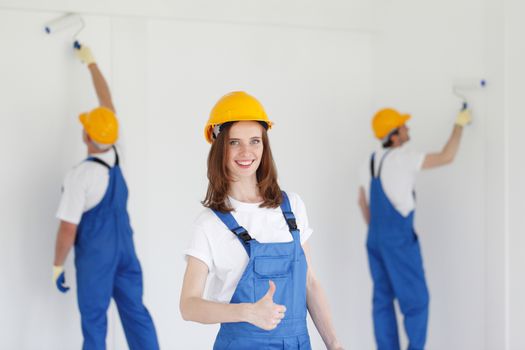 Female worker gives thumbs up in front of two painters