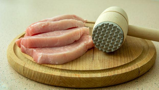 Raw pieces of loin on a wooden board and a meat mallet