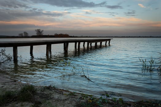 Wooden bridge towards the lake and dark evening clouds, october view