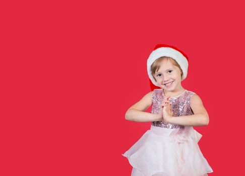 Adorable funny cacusian little girl in santa hat claps his hands for a gift celebrating happy New Year isolated on red background. Merry Christmas presents shopping sale.