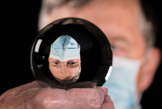 Senior man wearing face mask against coronavirus and reflected in fortune telling glass ball. Concept of people choosing responsibility in election