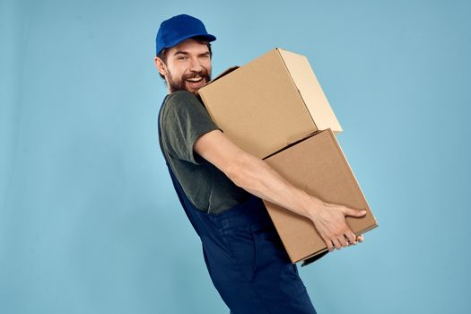 Man in working uniform with boxes in hands delivery service blue background. High quality photo