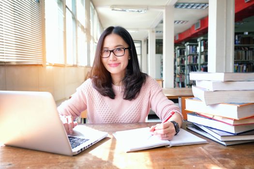 Young woman taking note and using laptop while studying in library