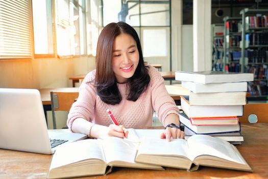 Young woman taking note and using laptop while studying in library