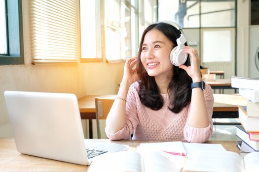 Young woman in a good mood listening to music  while studying in a library