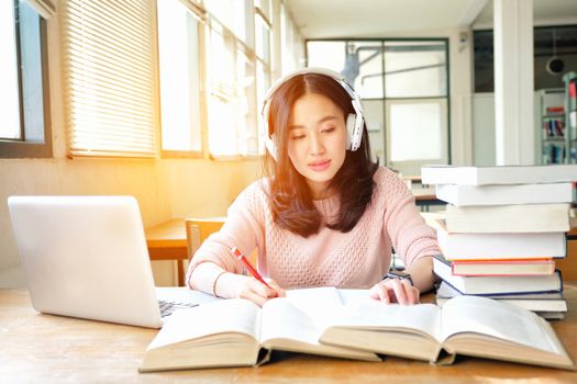 Young woman in a good mood listening to music  while studying in a library