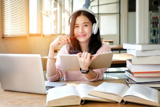 Young woman in a good mood listening to music  while studying in a library