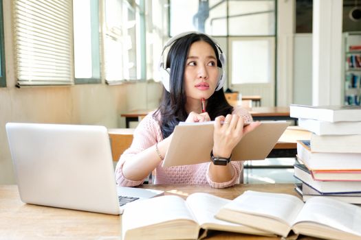 Young woman in a good mood listening to music  while studying in a library