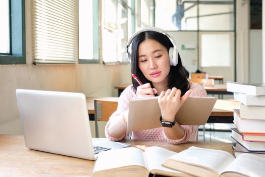 Young woman in a good mood listening to music  while studying in a library