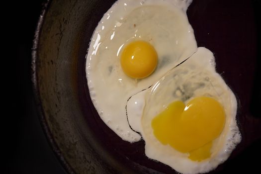 A fried egg in a frying pan on a white background.Close-up photo of two scrambled eggs in black frying pan