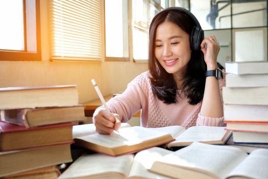 Young woman in a good mood listening to music  while studying in a library