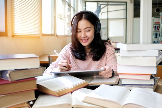 Young woman in a good mood listening to music  while using tablet in a library