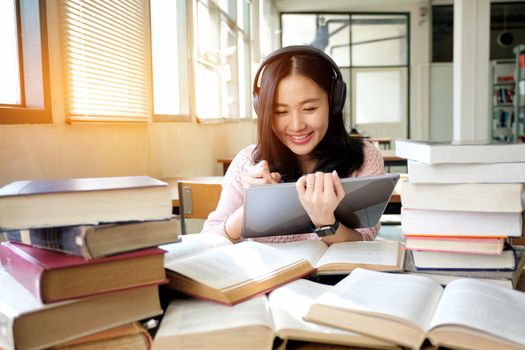 Young woman in a good mood listening to music  while using tablet in a library