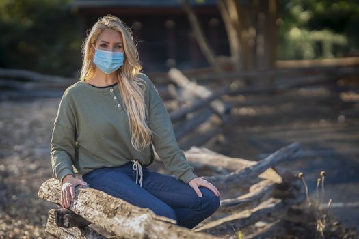A gorgeous blonde model poses outdoors in her fall clothes wearing a mask during the COVID-19 Pandemic