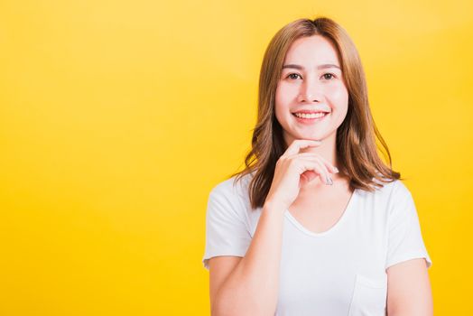 Portrait Asian Thai beautiful young woman wearing white t-shirt standing chin handle relaxed thinking about something about the question studio shot, isolated on yellow background with copy space