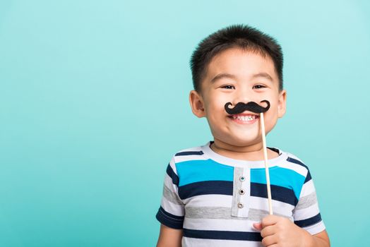 Funny happy hipster kid holding black mustache props for the photo booth close face, studio shot isolated on a blue background, Men health awareness, Prostate Cancer Awareness