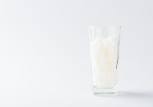 A glass full of white sugar cube sweet food ingredient, studio shot isolated on white background, health high blood risk of diabetes and calorie intake concept and unhealthy drink