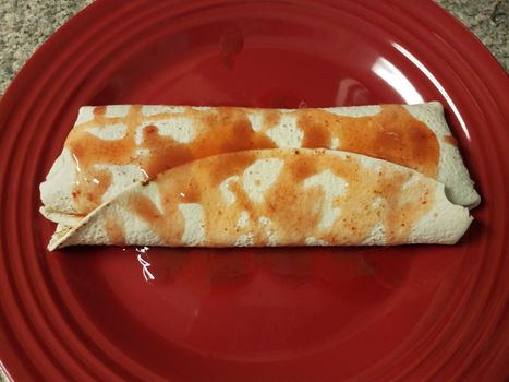 burrito with spicy hot sauce on red plate on counter