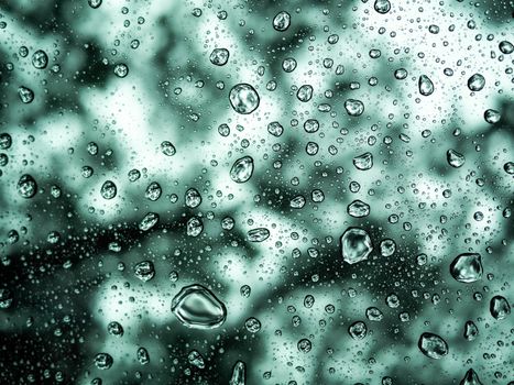 Rain drops or water droplets on clear glass on a blurred nature background.