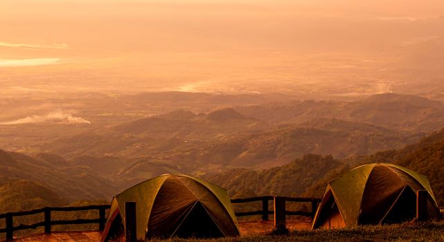 Two tents stands against the background of beautiful mountain landscape with the warm sunset light.