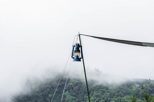 A kerosene lamp hanging on a pole in front of the tent against the background of beautiful mountain landscape and the morning mist.