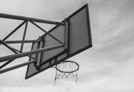The back image of the basketball board hoop with the loop on the sky background. Black and white style tone.