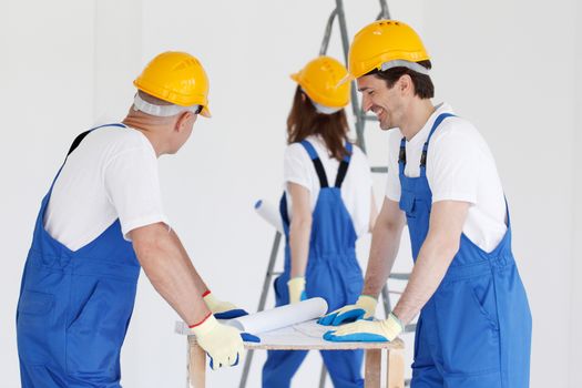 Workers in blue uniform and yellow hardhats with blueprint working at construction site