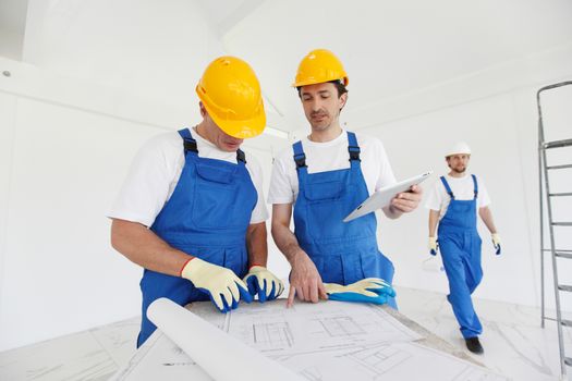 Workers in blue uniform and yellow hardhats with blueprint working at construction site