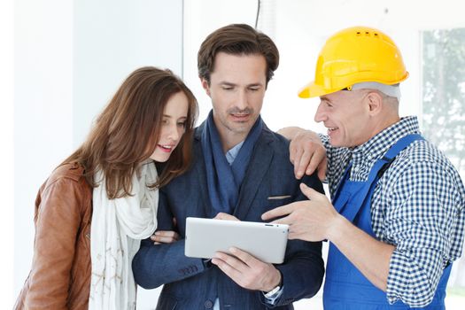 Worker and couple using tablet pc at construction site planning renovation house design plans