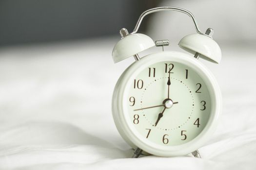 Alarm clock on wooden table for wake up time with light from window, selective focus