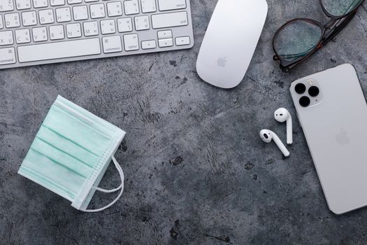 working space with Apple computer keyboard & mouse, iPhone 11 Pro Max, Airpods, eyeglasses and disposable face mask, concept of flu prevention in COVID-19 situation