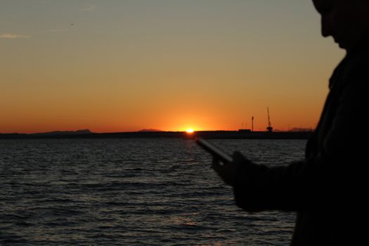 Santa Pola, Spain- November 10, 2017: Woman silhouette looking at her mobile phone at sunset on the beach