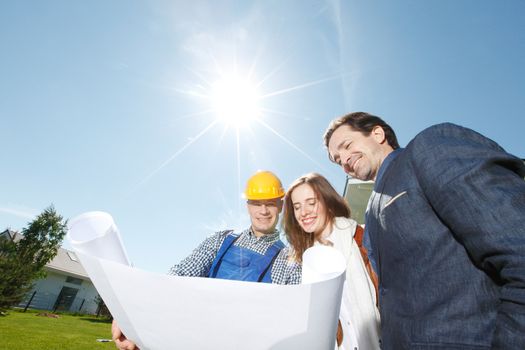 Foreman showing holding house design construction plan to a happy young couple new house real estate concept