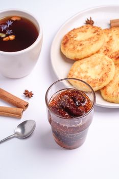 Cottage cheese fritters with fig jam and hot black aromatic tea, Christmas breakfast mood with anise and cinnamon on white background, angle view