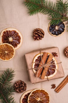 Christmas composition with handmade kraft paper gift box, dried citrus slices, cinnamon, anise, pine cones and fir tree branches, top view close up