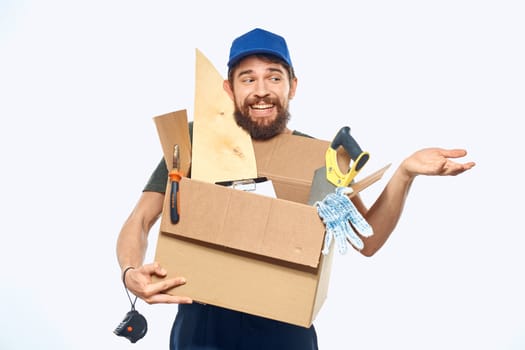 Worker man in uniform with a box in his hands tools delivery service light background. High quality photo