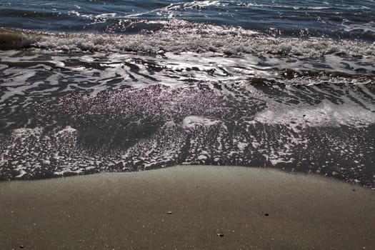 Waves, light and sand texture on the beach in the morning
