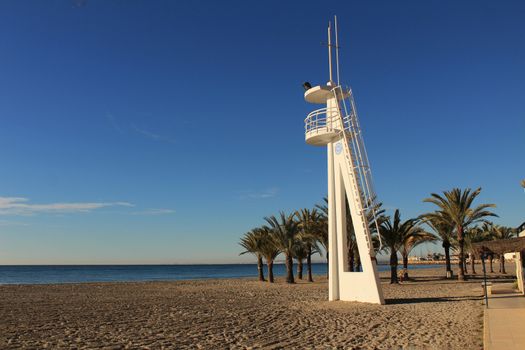 Santa Pola, Spain- February 16, 2018: Lifeguard tower on a quiet and lonely beach in a sunny day in southern Spain, Alicante. Palm trees in the background.