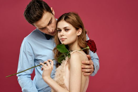 enamored man and woman with a red flower on a pink background hug each other Copy Space. High quality photo