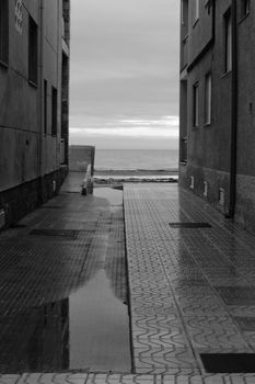 Lonely Little street between buildings facing the sea after a rainy day. Black and white Photography