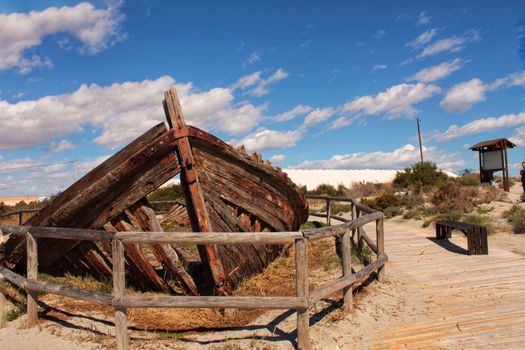 Old abandoned boat on the beach in Santa Pola. Salinas in the background under blue sky