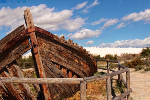 Old abandoned boat on the beach in Santa Pola. Salinas in the background under blue sky
