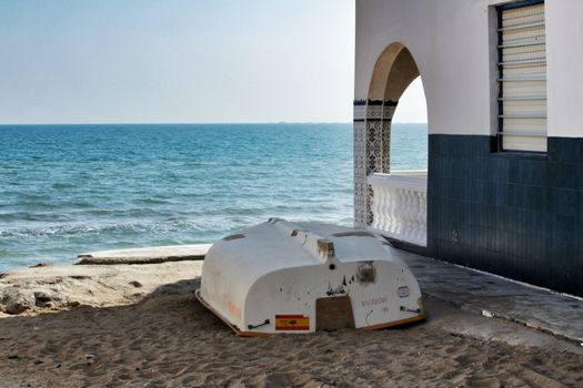 Alicante, Spain- February 9, 2020: White boat next to beautiful white and blue tiled house on the shore in Alicante in a clear day of winter