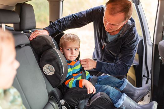 Father fastening safety belt for his baby boy in his car seat. Children's Car Seat Safety